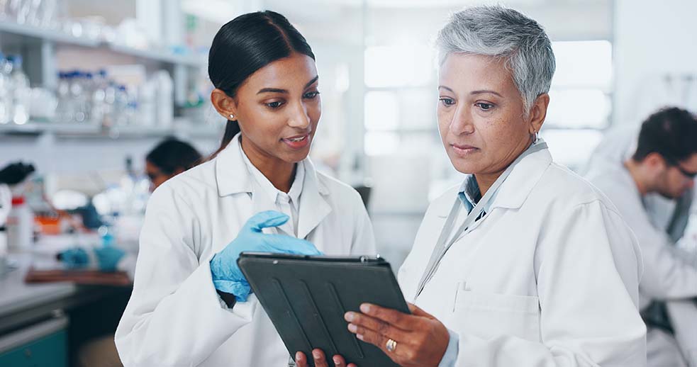 Two females in white lab coats looking at an ipad about women's health leads